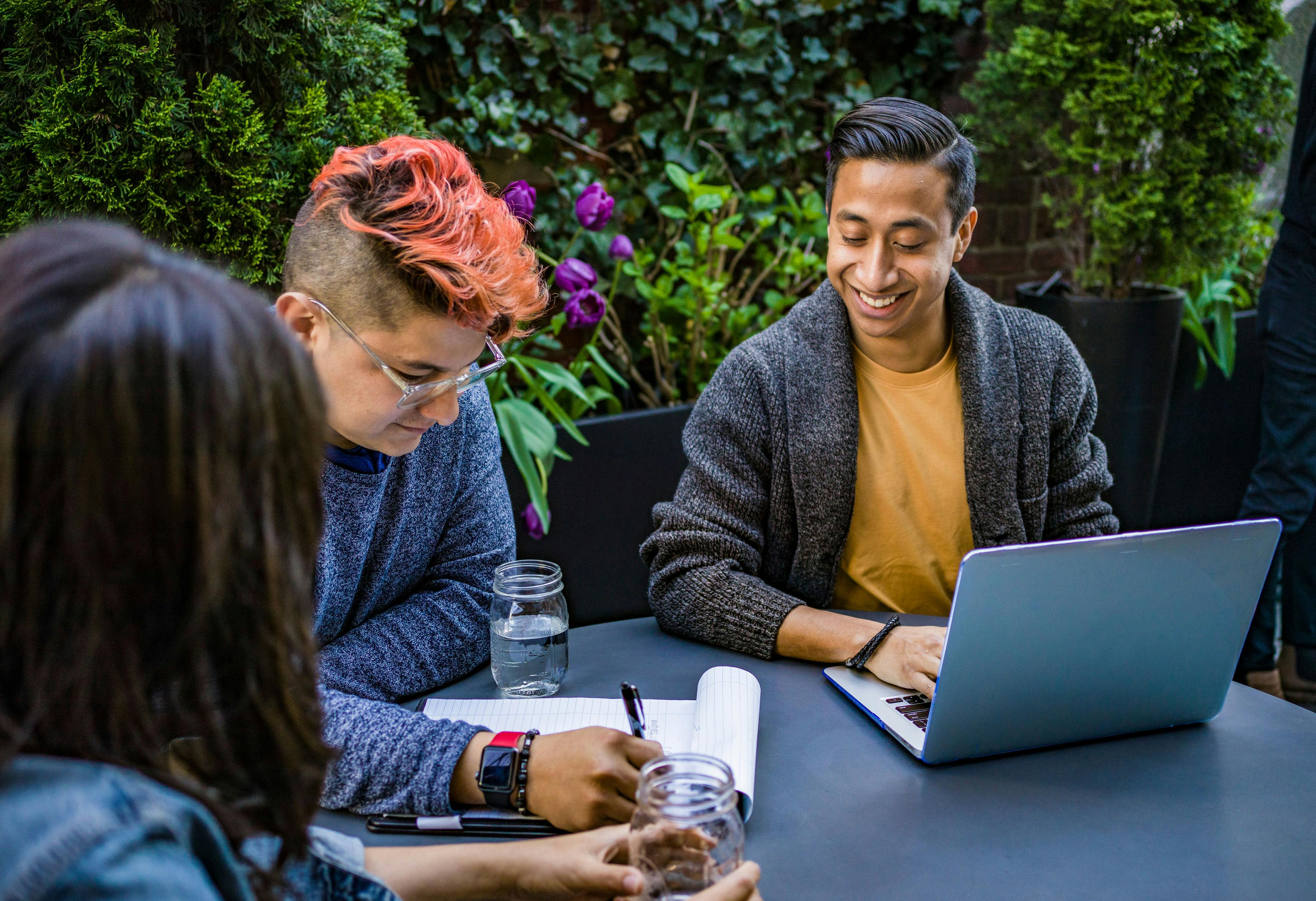 man in orange crew neck shirt using laptop beside two people