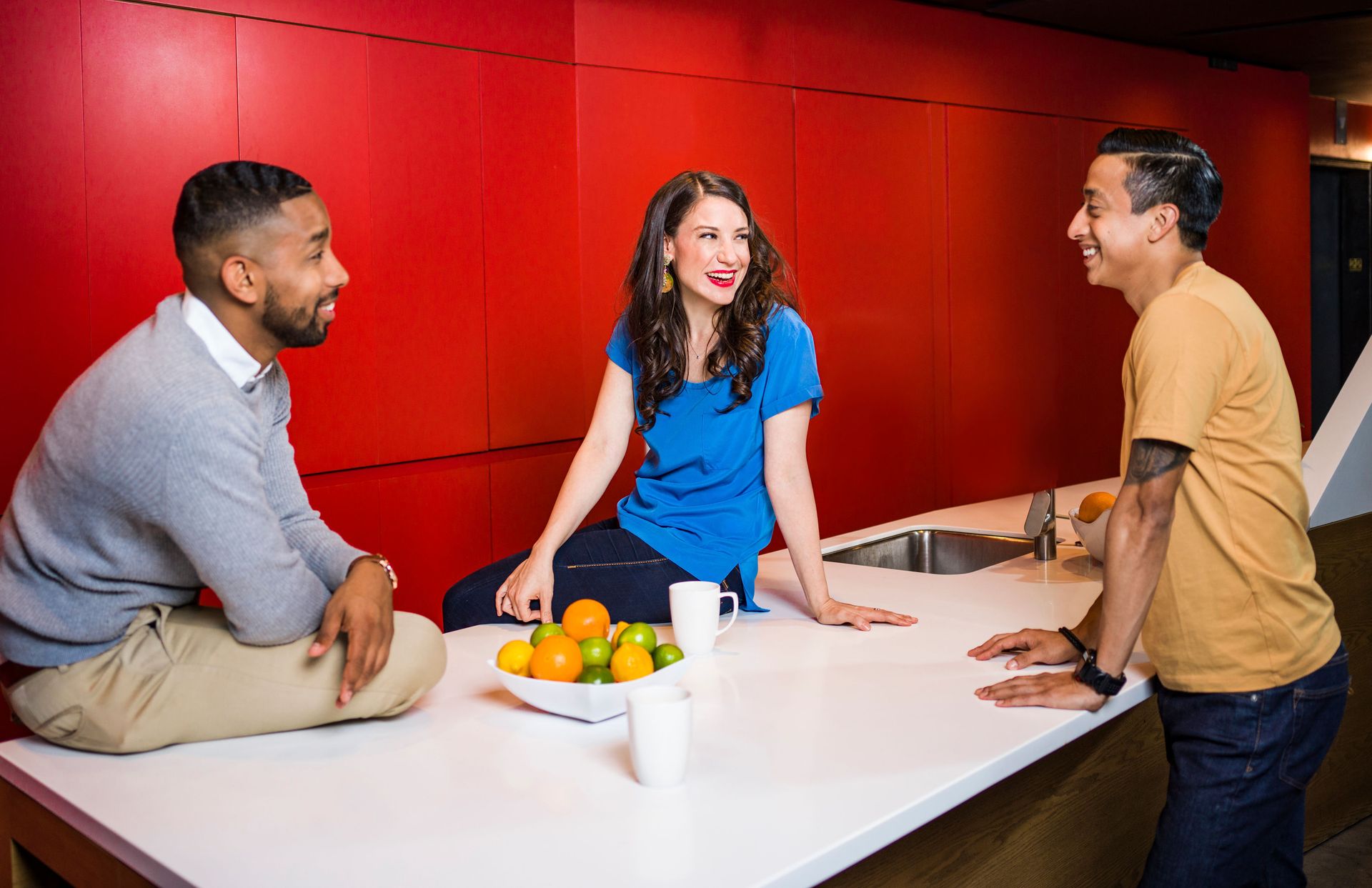 Three adults enjoy a friendly conversation in a modern kitchen with bold red decor.