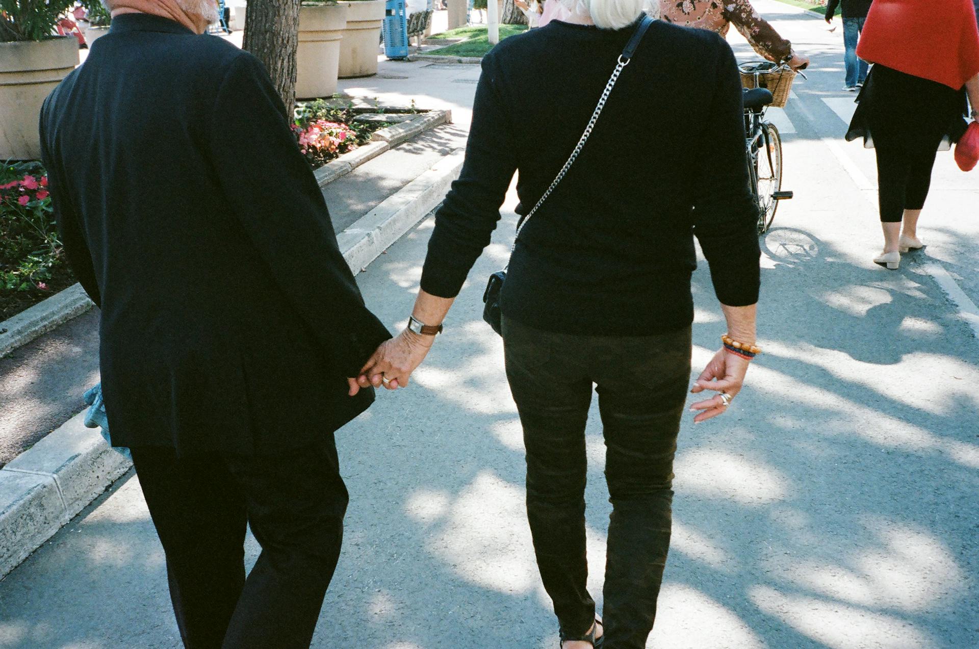 A senior couple affectionately holding hands while strolling down a sunlit urban street.