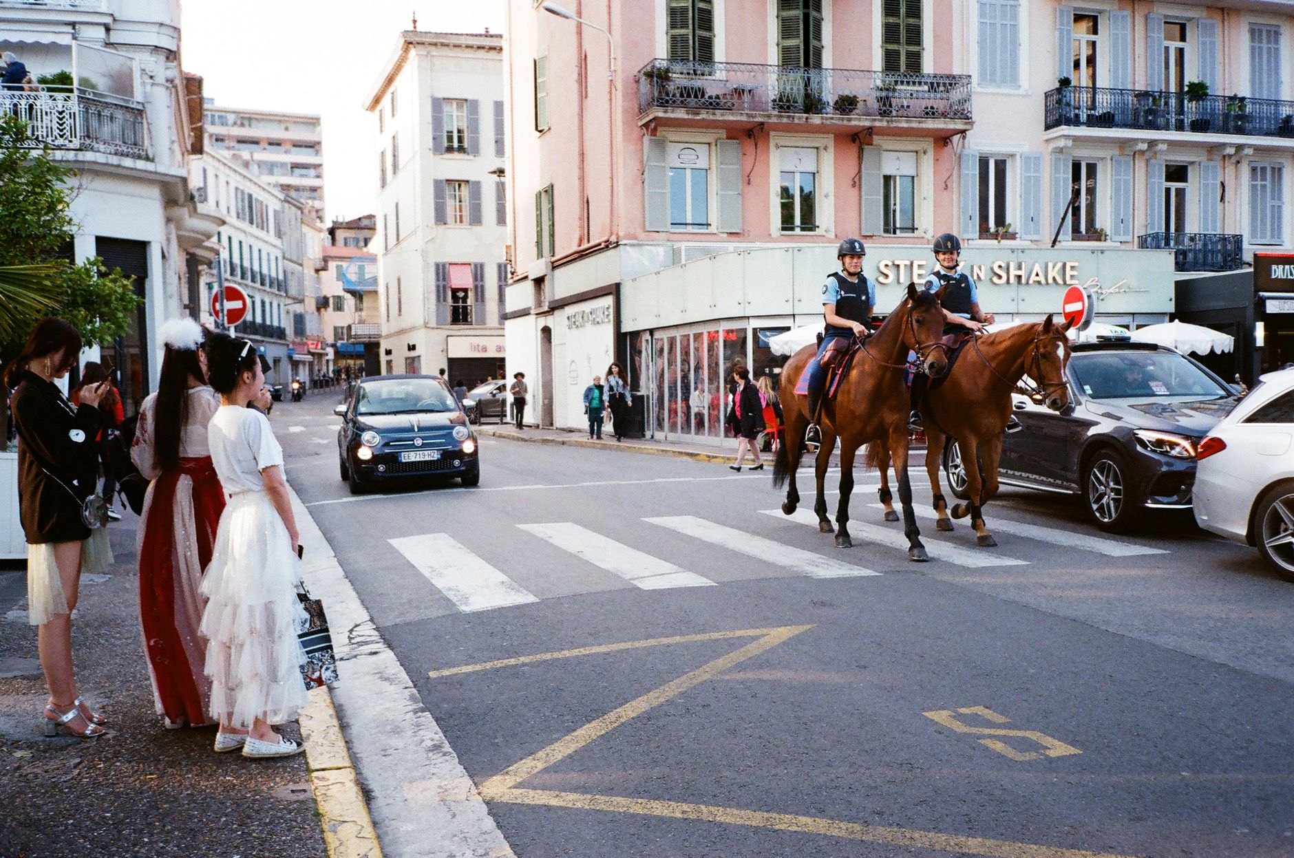 City street with mounted police, pedestrians, and a mix of cars and historic buildings.