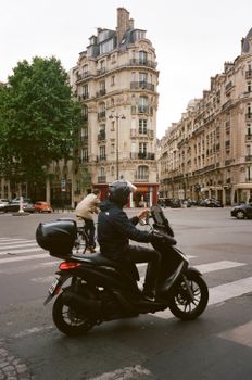 A motorcyclist rides through a historic city intersection with classic architecture.