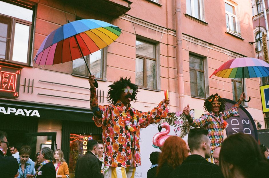 Colorful street festival featuring performers with rainbow umbrellas and vibrant outfits.
