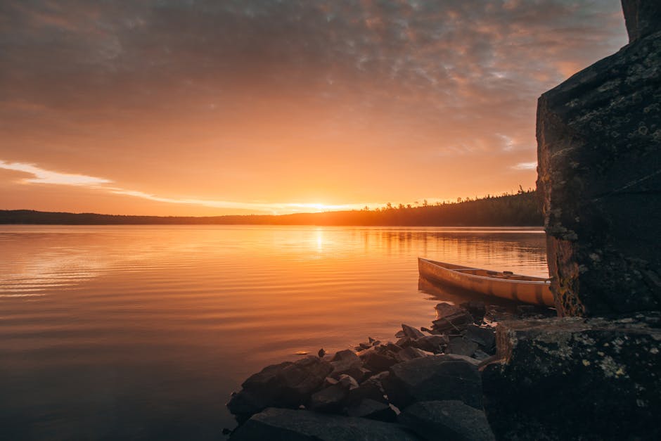 Luontoaktiviteetit ja Vesiharrastukset Luontoaktiviteetit ja Vesiharrastukset - A tranquil sunset over a lake in Ely, Minnesota, featuring a canoe by the rocky shor