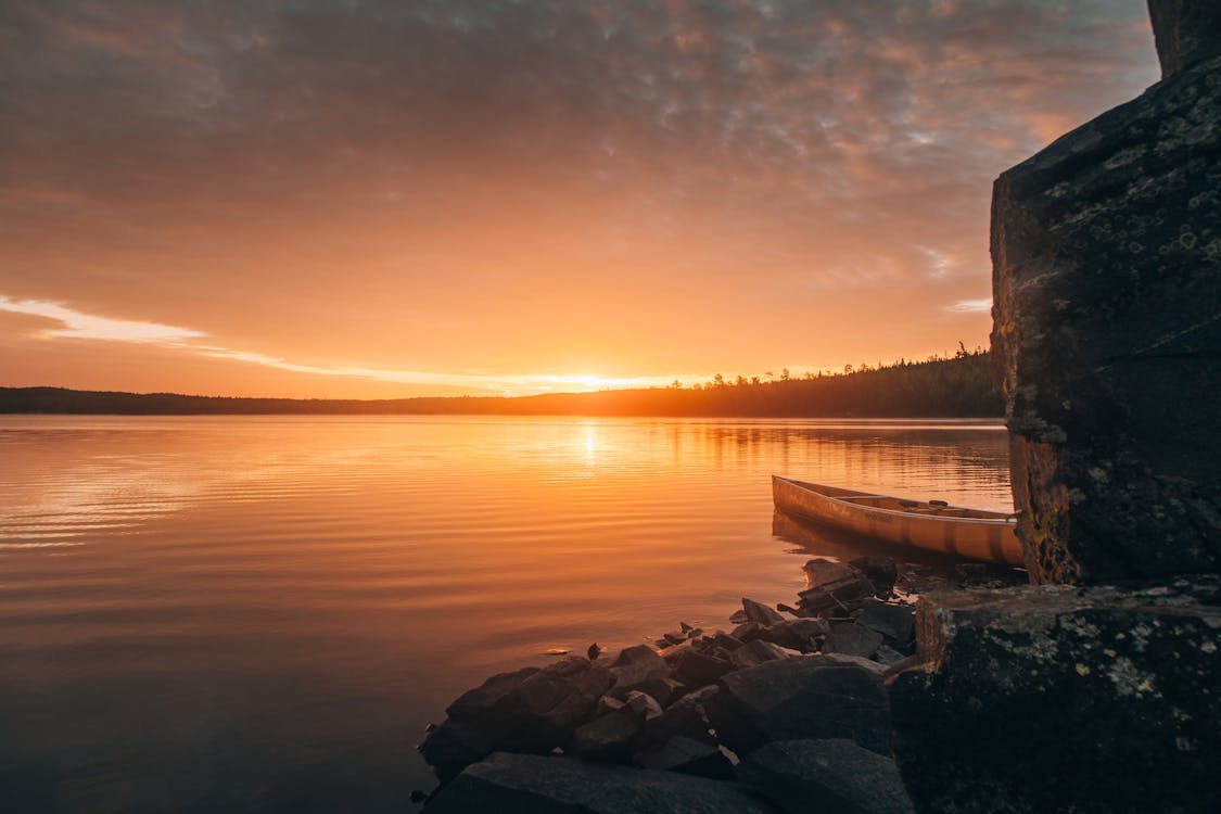 Free A tranquil sunset over a lake in Ely, Minnesota, featuring a canoe by the rocky shore. Stock Photo