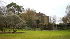 一座雄伟的历史豪宅坐落在英国乡村，周围环绕着郁郁葱葱的花园