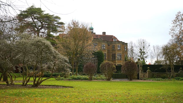 一座雄伟的历史豪宅坐落在英国乡村，周围环绕着郁郁葱葱的花园