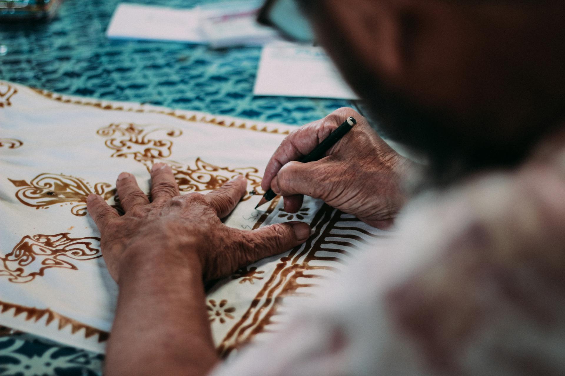 Skilled artisan handcrafting detailed batik patterns on fabric using precision tools.