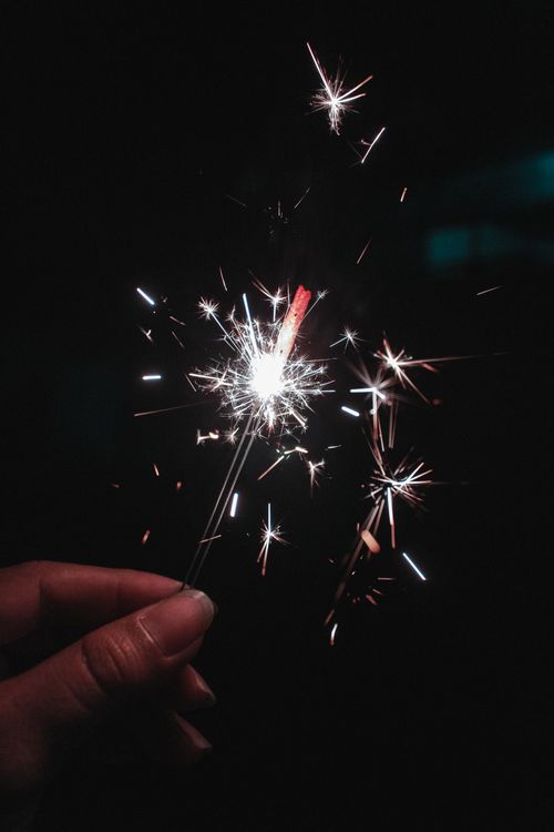Free A hand holding a lit sparkler emitting bright sparks in the dark, perfect for festive celebrations. Stock Photo