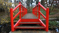 一座充满活力的红色木桥横跨在宁静的秋季公园中流淌的溪流上