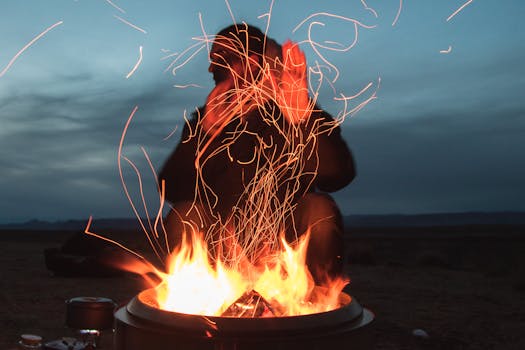 A person enjoying warmth by a vibrant campfire at twilight, sparks flying into the night sky.