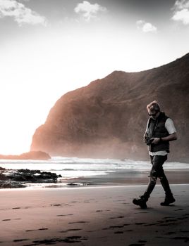A contemplative man walks along a picturesque New Zealand beach at sunset, embracing nature's serenity.