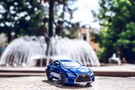 Blue Die-cast Toy Car Across Outdoor Fountain