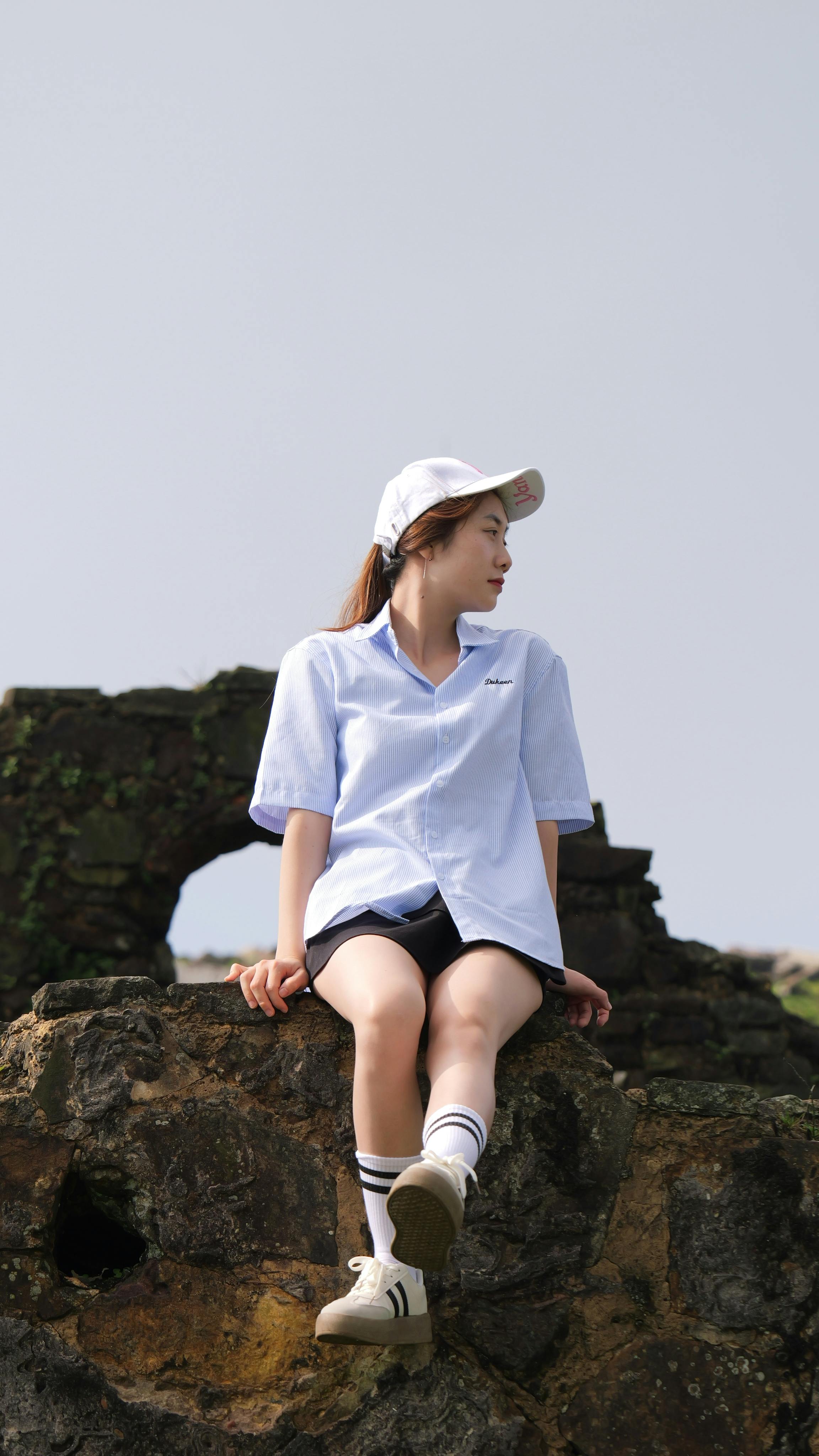 Fashionable young woman in casual attire sitting outdoors on rocky terrain, exuding a modern style.