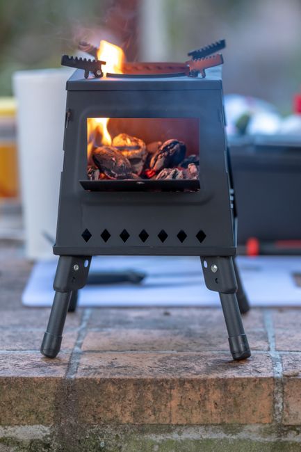 A compact dual-burner camping stove set up on a picnic table with cookware and ingredients, ready for outdoor cooking