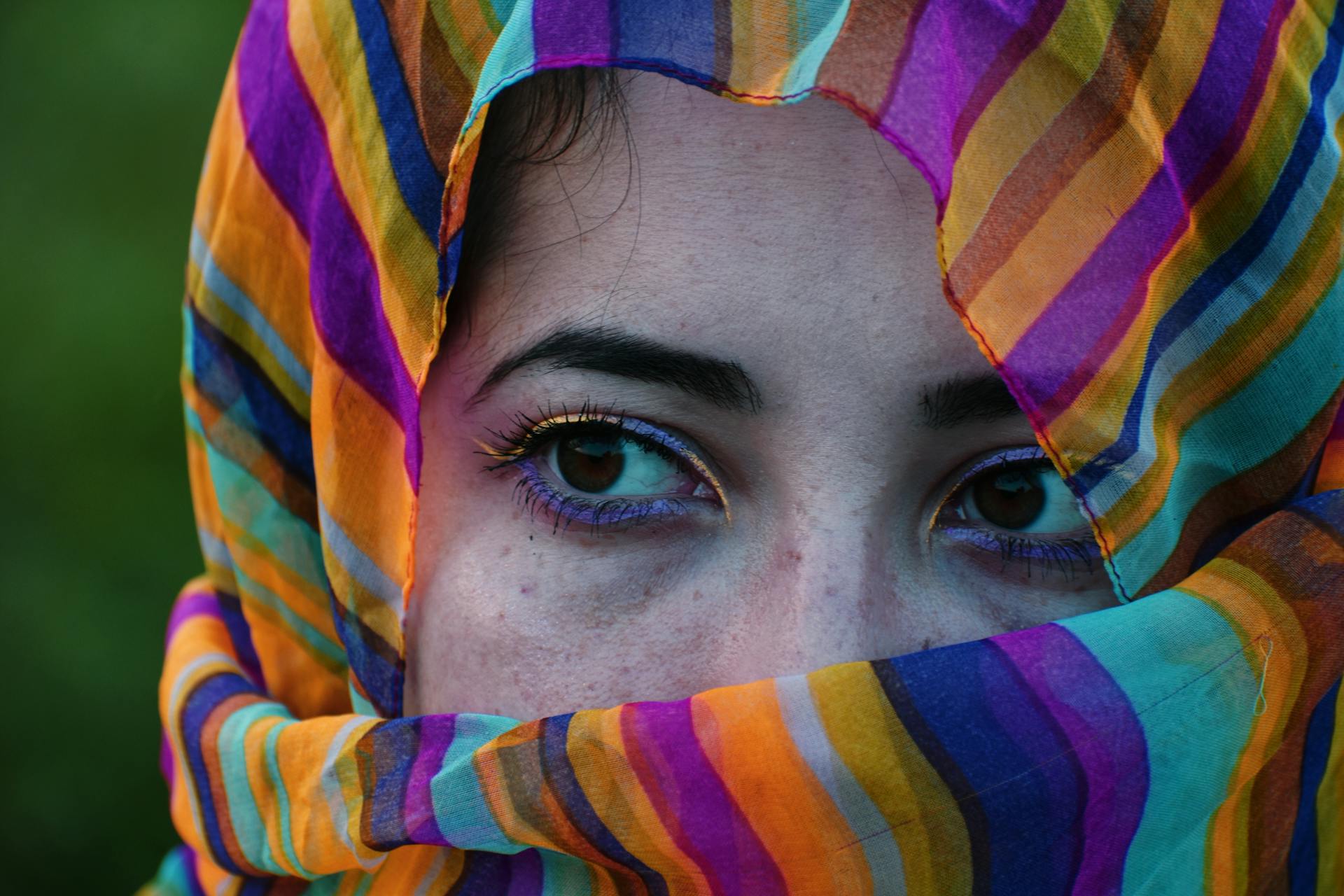 Close-up of a woman's eyes with a vibrant, striped headscarf covering her face.