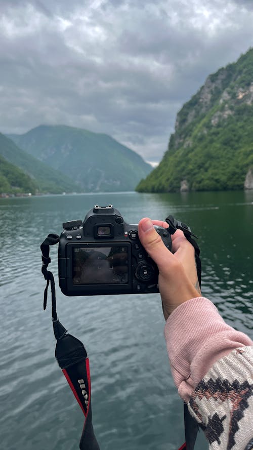 A hand holding a Canon camera taking a photo/filming a beautiful lake scenery 