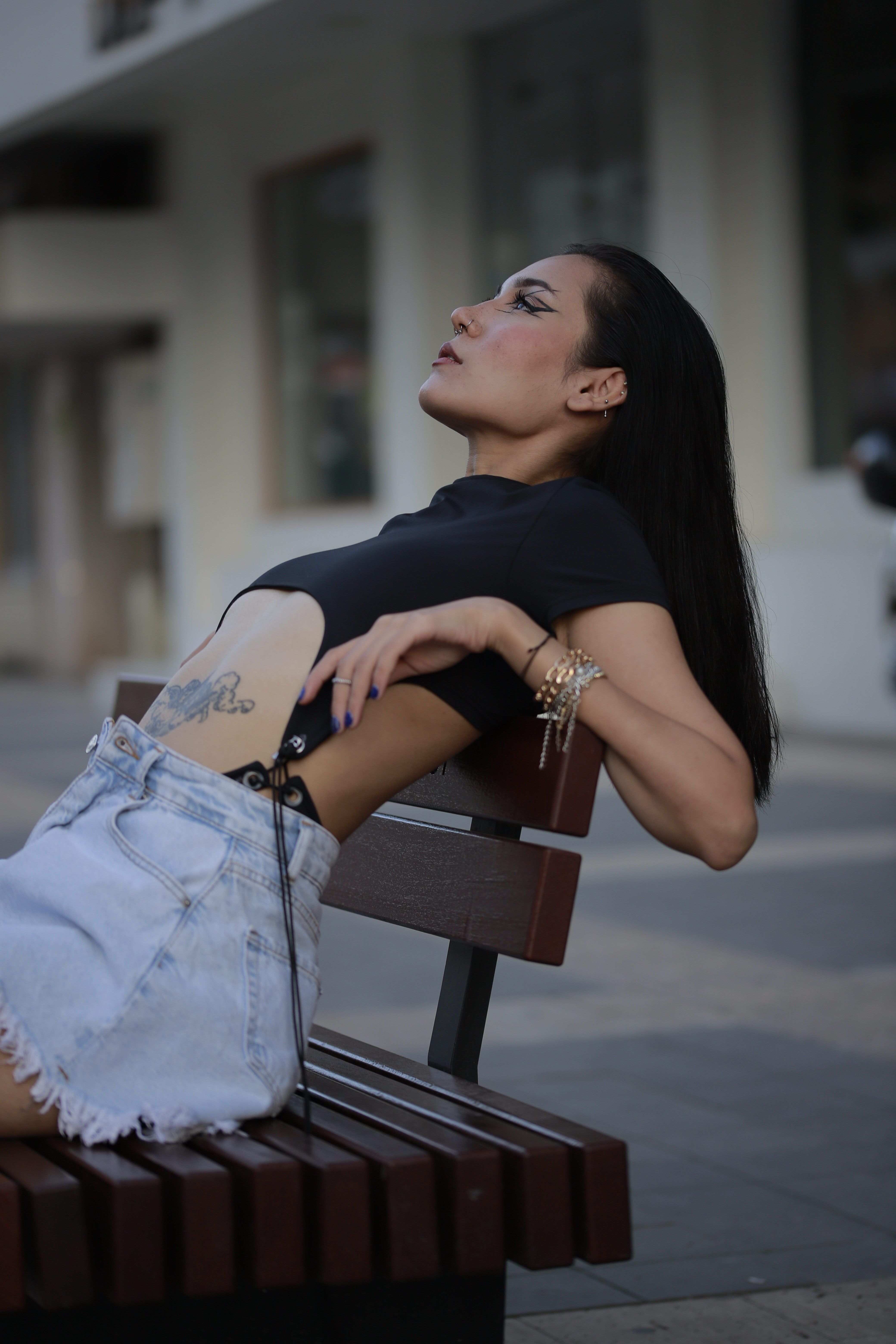 Fashionable woman in casual wear leaning back on a bench in the city.