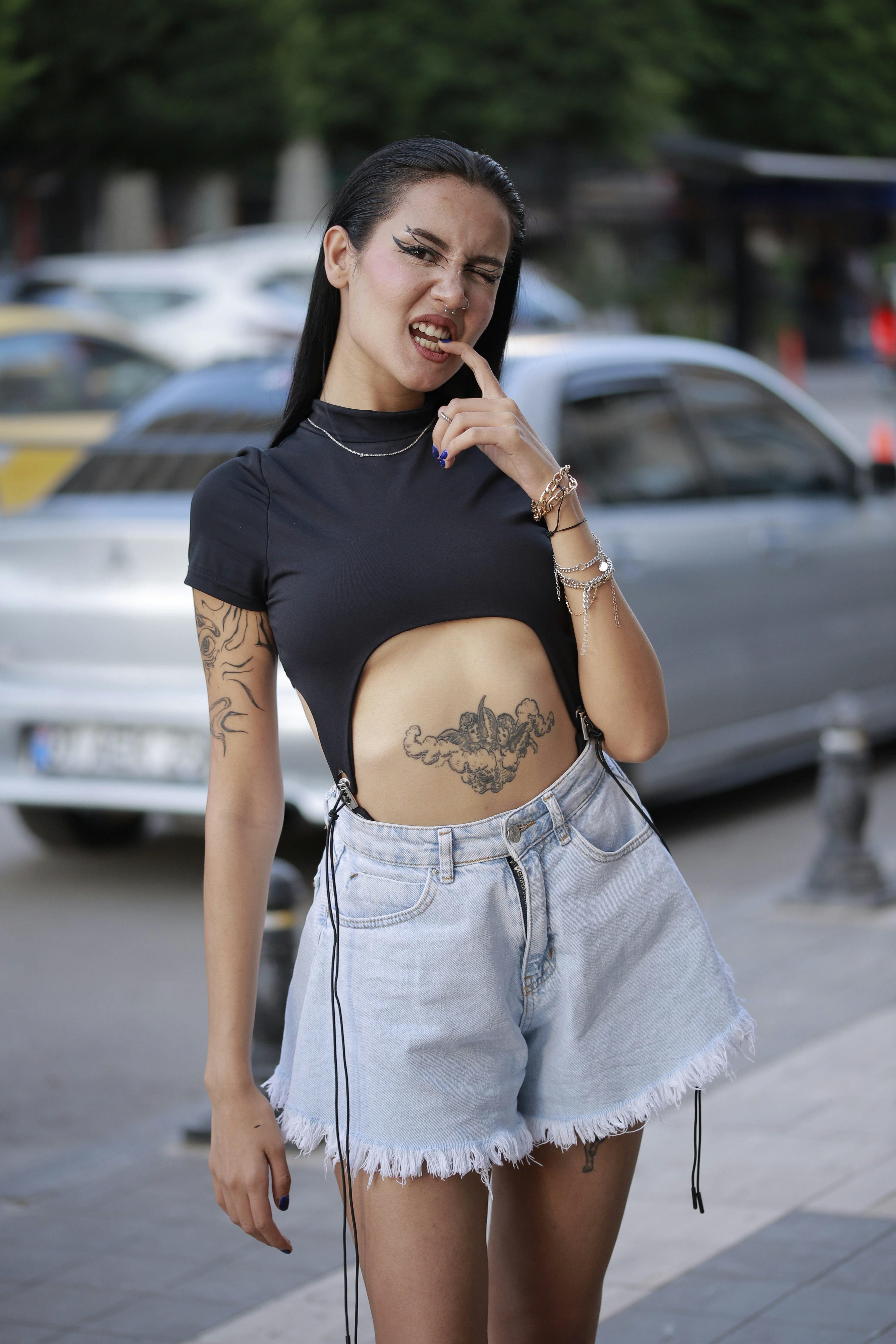 Stylish urban portrait of a woman in denim shorts, showcasing tattoos, on a city street.