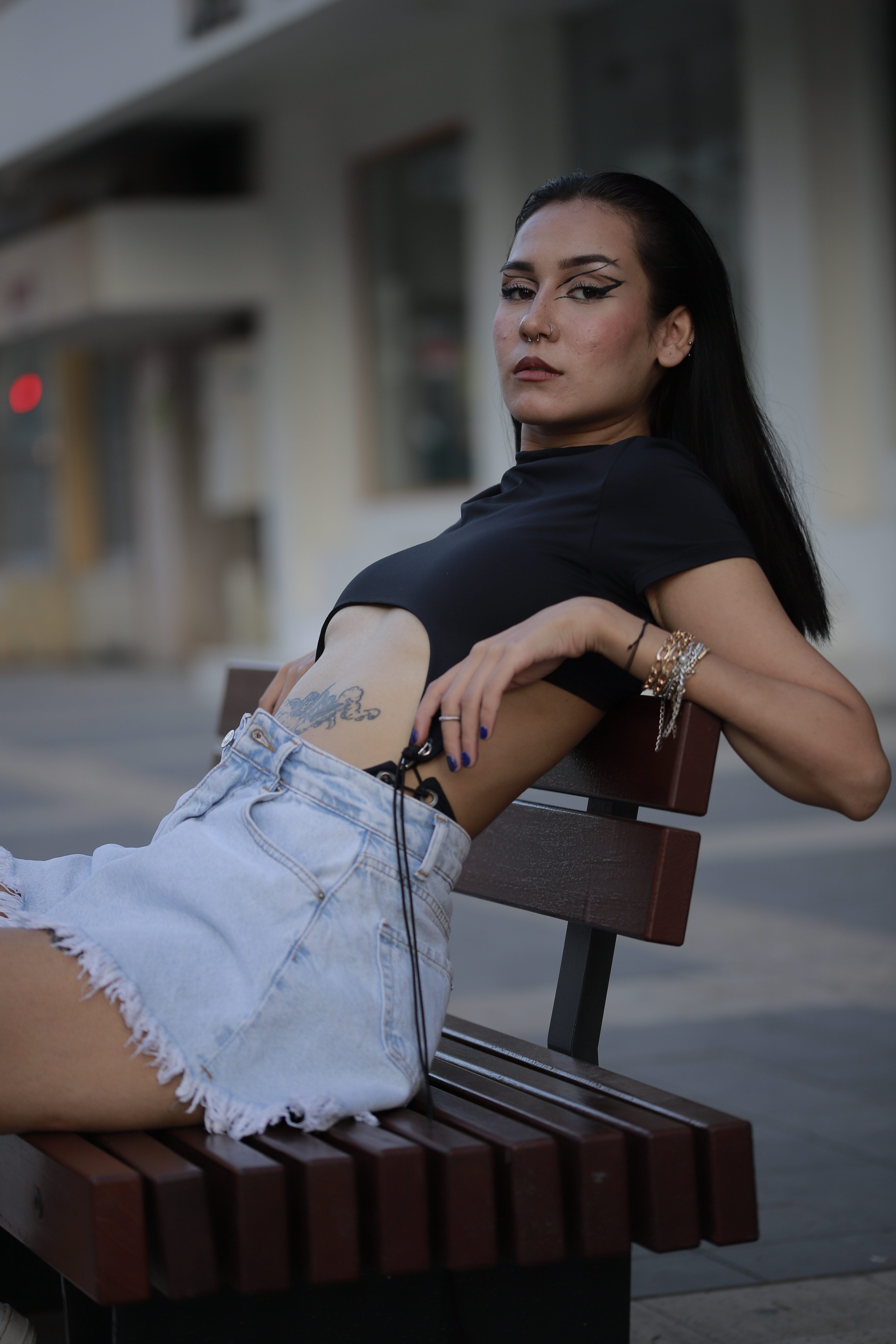 Stylish woman in denim shorts posing on a bench in an urban setting.
