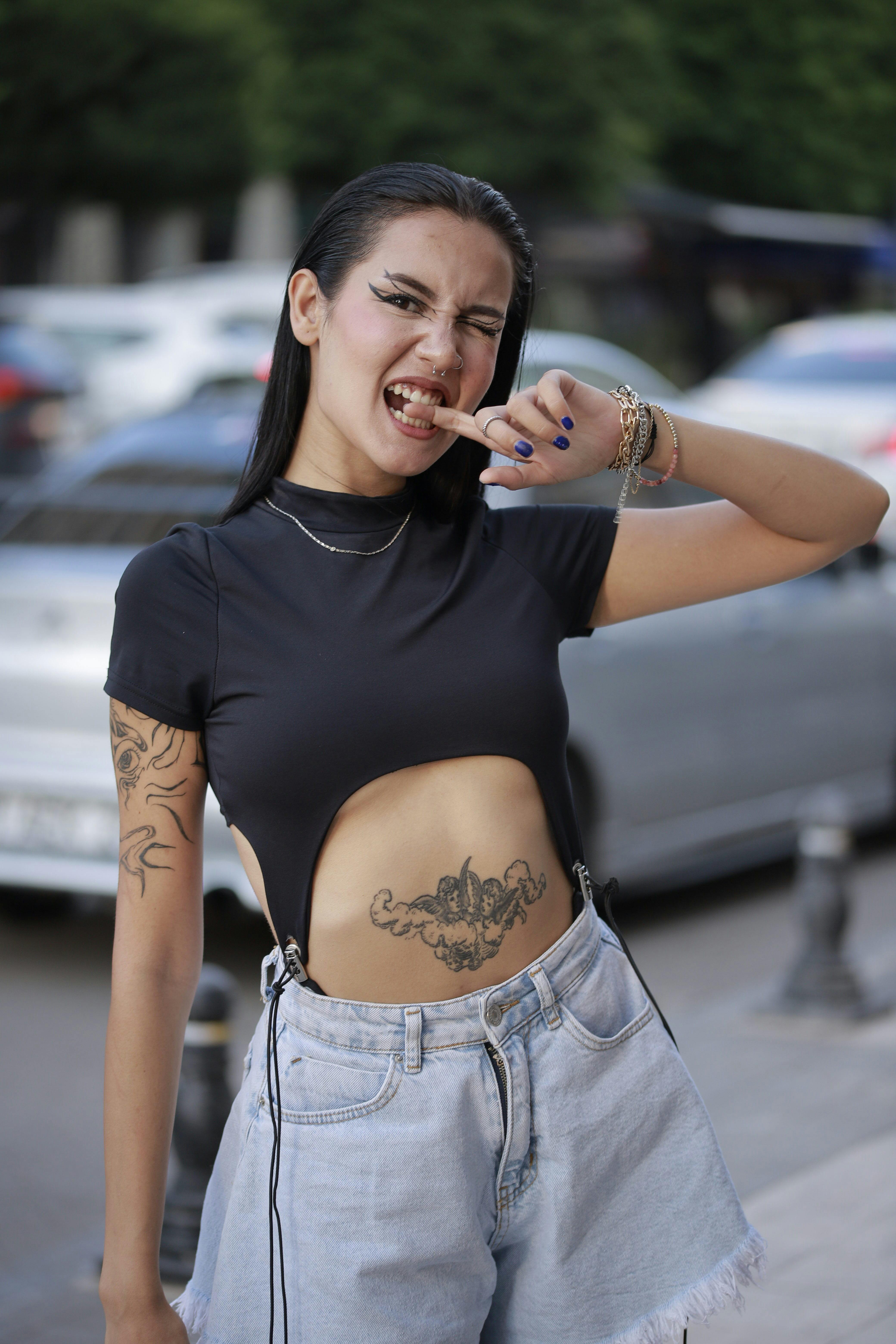 Stylish woman with tattoos poses playfully in urban setting, showcasing edgy fashion.