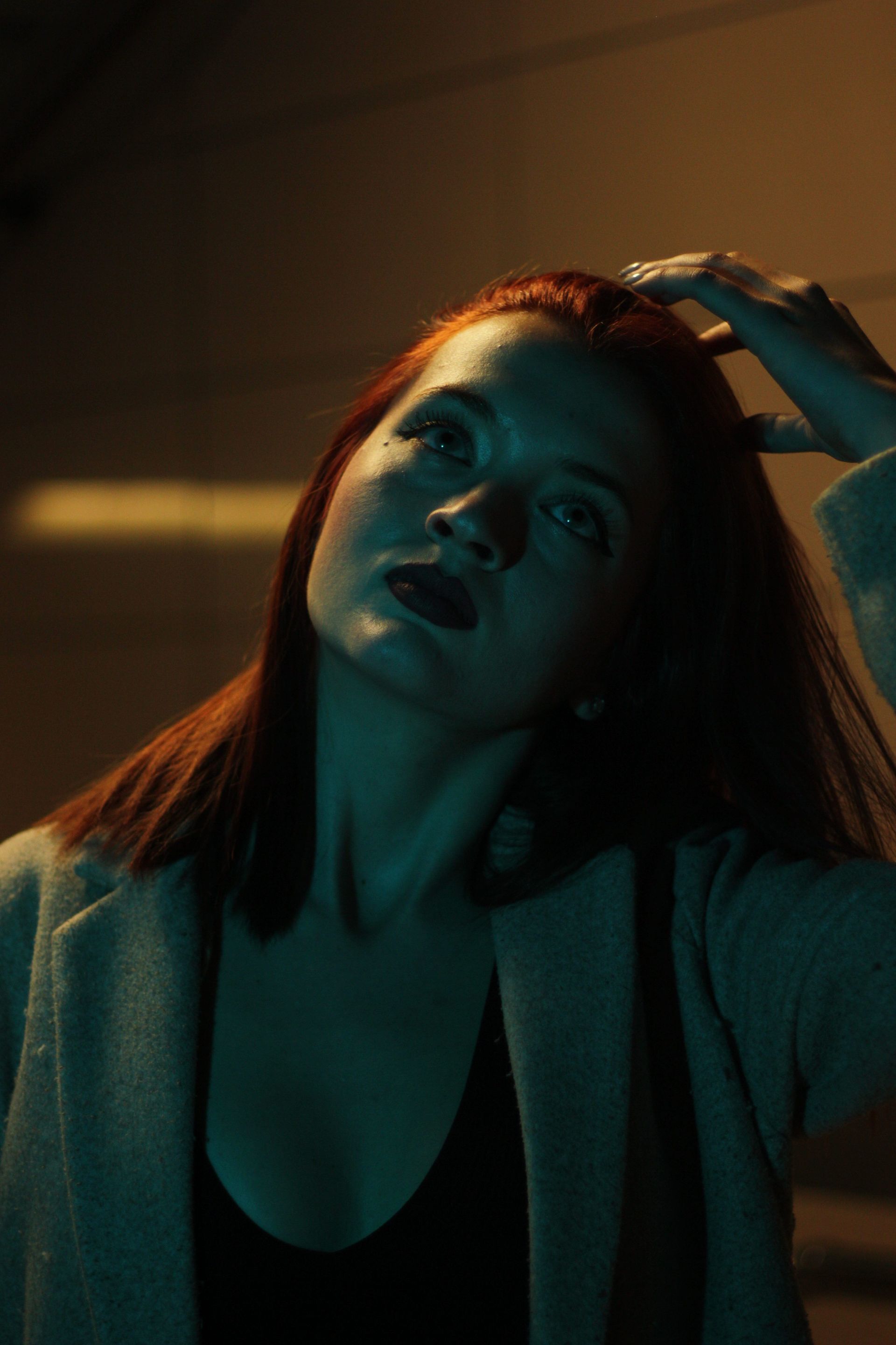 A dramatic, moody portrait capturing a red-headed woman under dim lighting