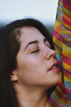 Close-up portrait of a woman with yellow eye makeup against colorful fabric.