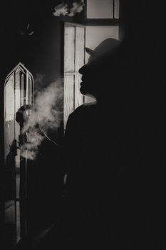 Dramatic silhouette of a man with a hat, indoors, enveloped in smoke.