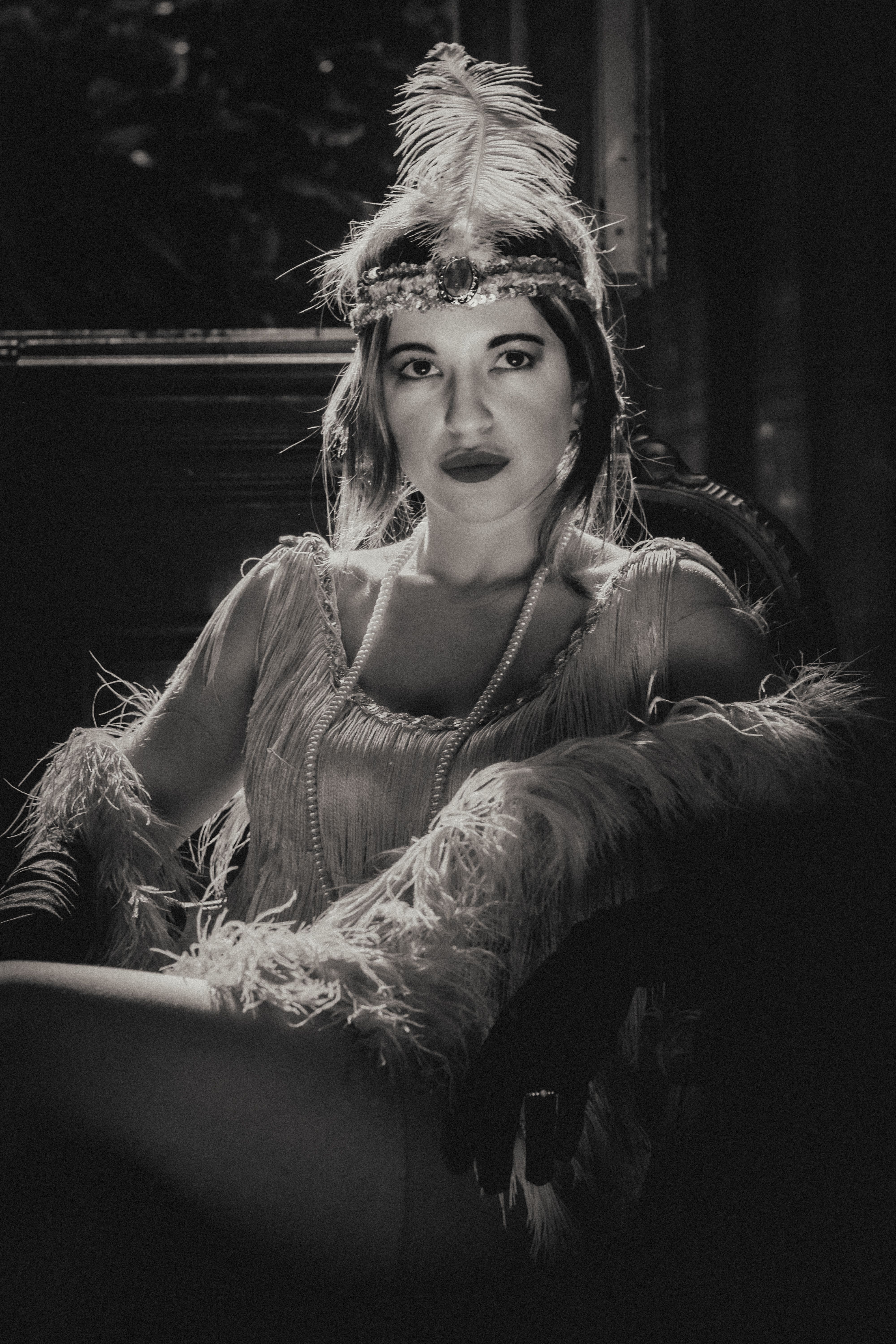 Elegant woman in flapper costume posing with feathered headpiece and pearls.