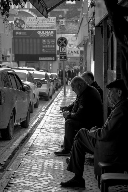 Free Black and white photo of elderly men sitting on a city sidewalk, capturing urban leisure and relaxation. Stock Photo