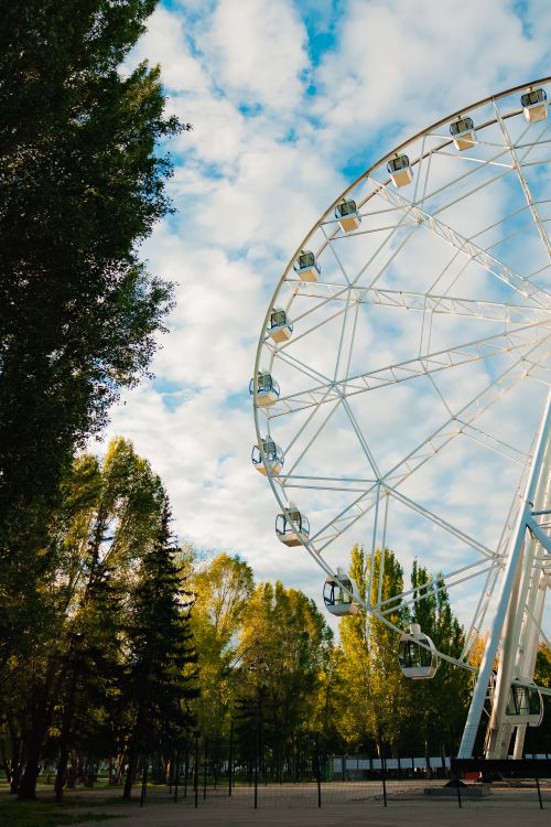 Free A large Ferris wheel stands tall in a lush park under a blue sky with scattered clouds. Stock Photo