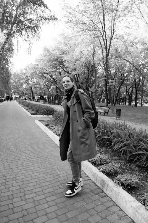 A woman in a coat and sneakers walking down a sidewalk