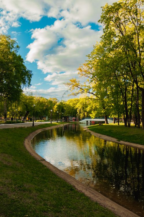 Free Tranquil park scene featuring a winding canal and vibrant spring foliage under a bright sky. Stock Photo