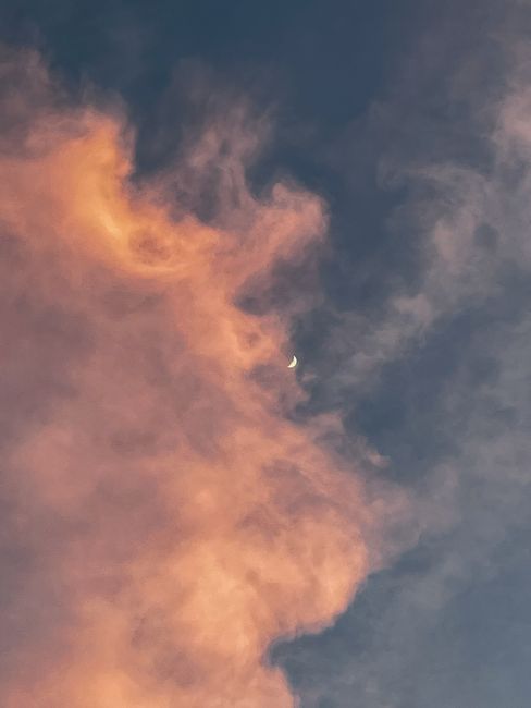 A crescent moon peeks through colorful sunset clouds, creating a dramatic sky scene.