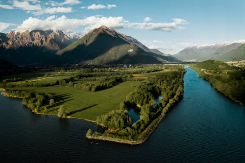 Picturesque landscape of calm river flowing through peaceful green valley surrounded by mountains under blue sky