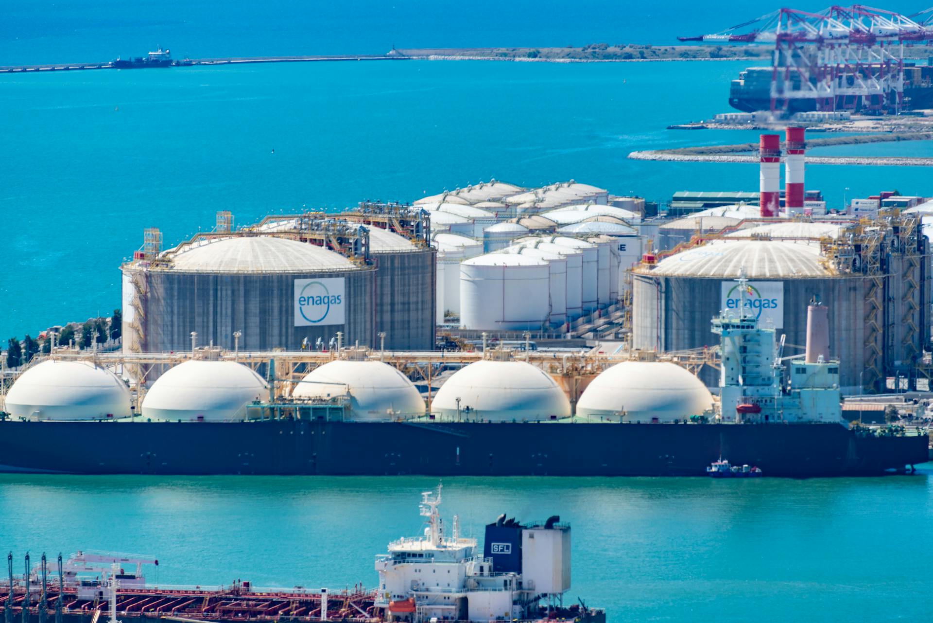 Aerial shot of a gas terminal featuring LNG storage tanks and tanker ships in turquoise waters.