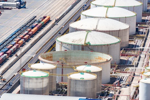Aerial shot of large oil storage tanks in an industrial district with adjacent railway tracks.