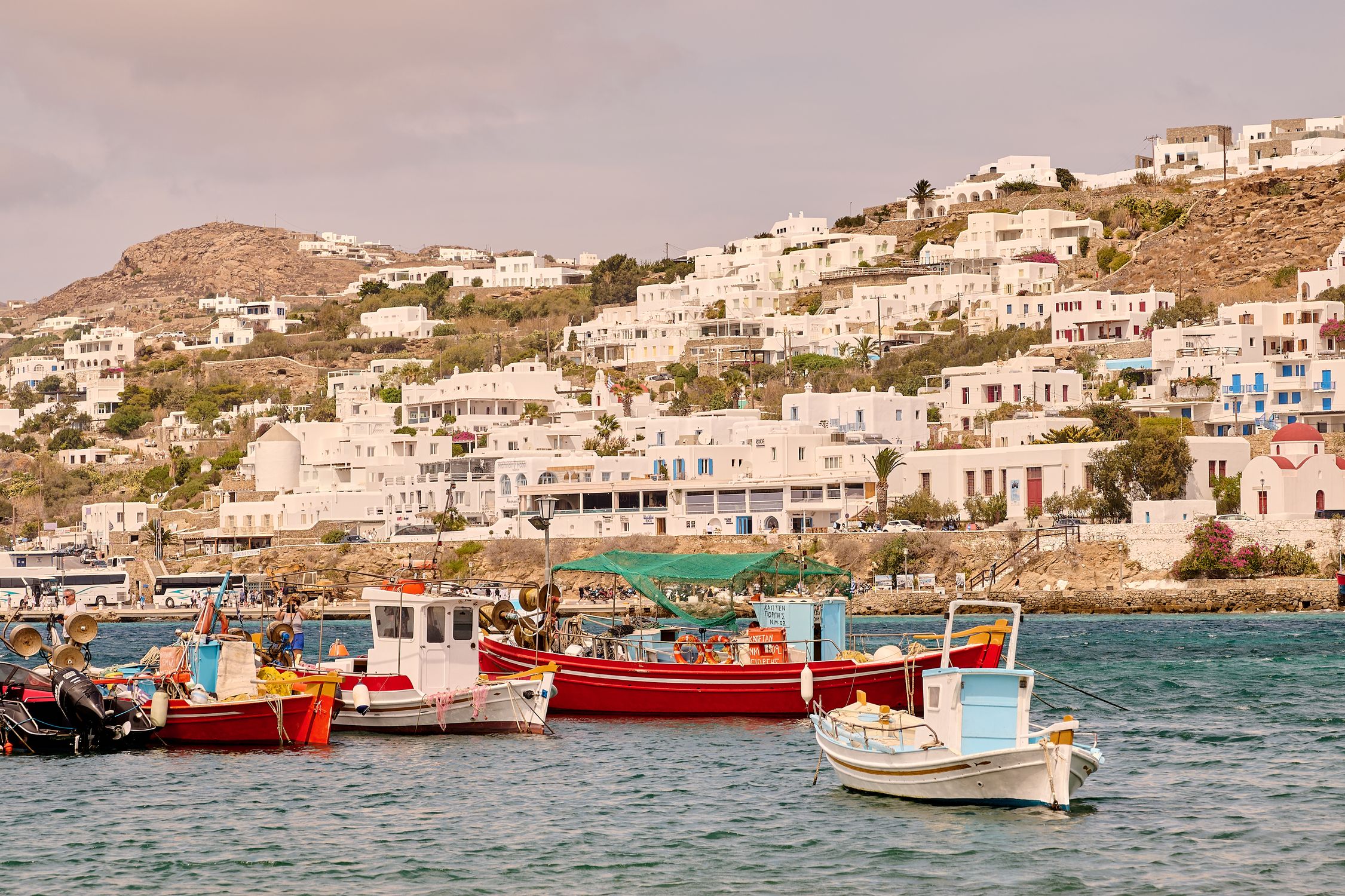 Charming white buildings and vibrant boats in Mykonos harbor on a sunny summer day.