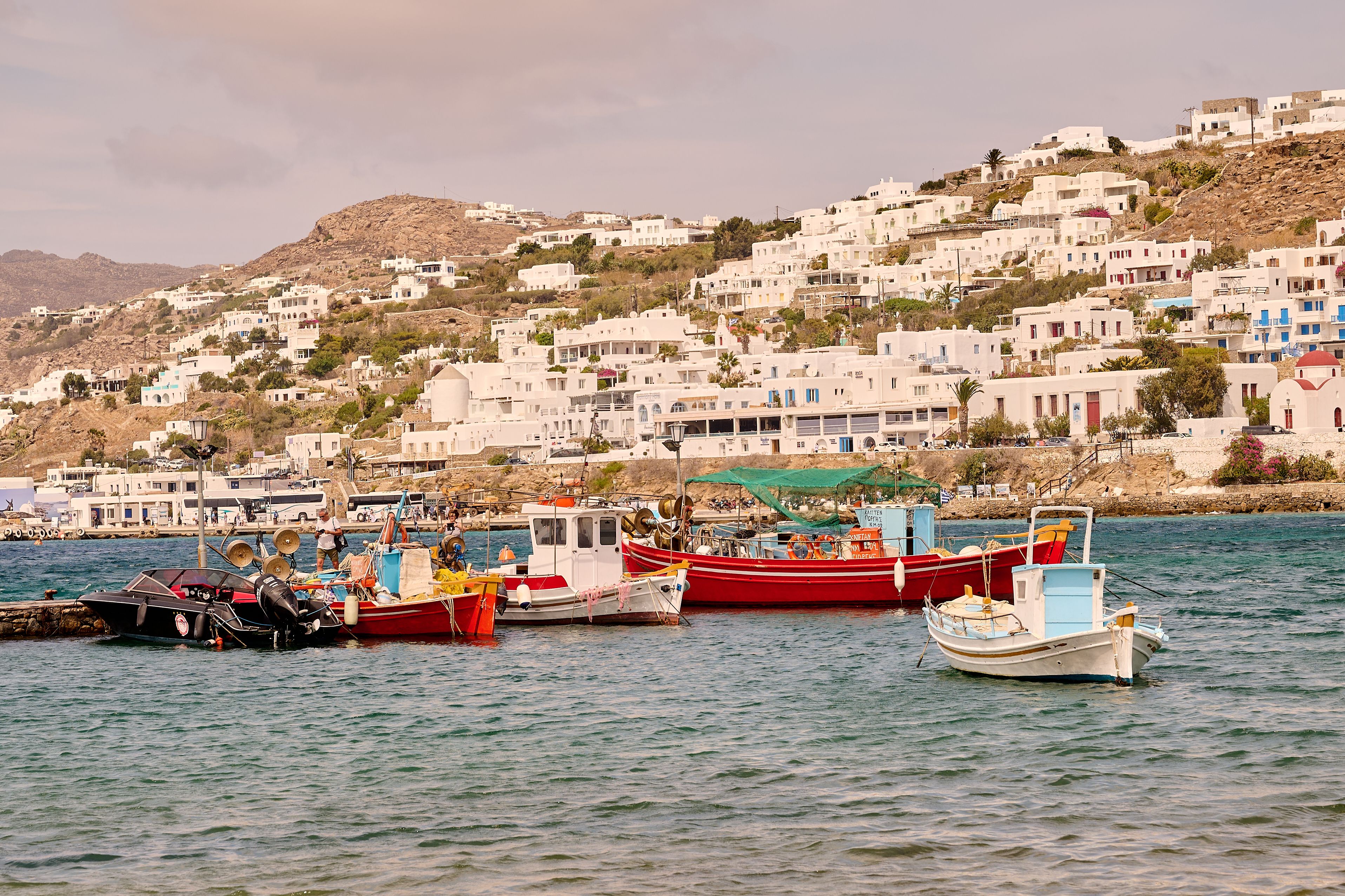 Free Charming view of Mykonos harbor with colorful boats and white hillside houses under summer sunlight. Stock Photo