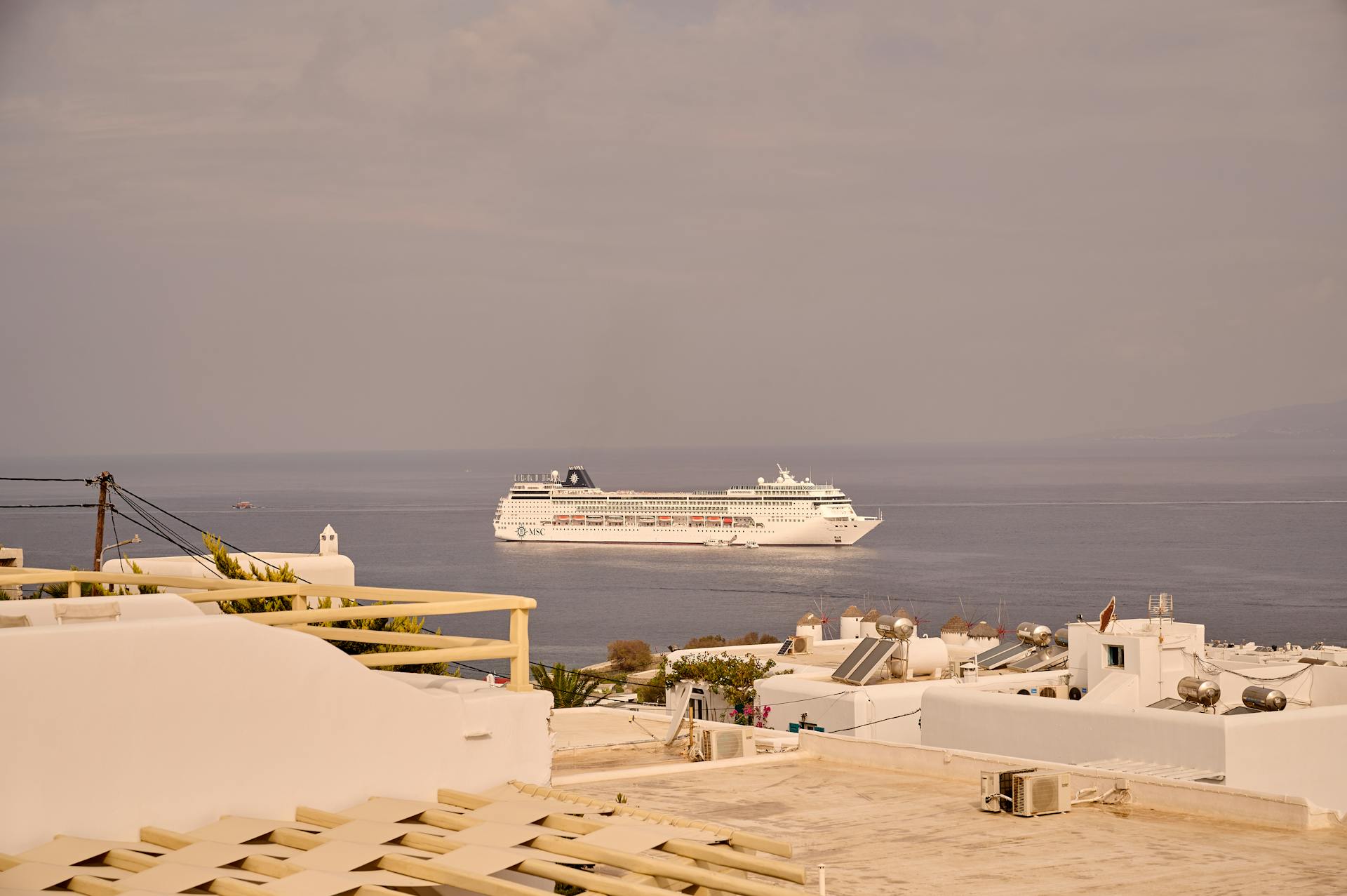 A cruise ship sails near a Mediterranean town, showcasing urban architecture and serene sea views.