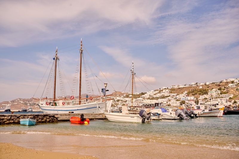 Peaceful view of Mykonos harbor with sailboats and colorful boats in sunlight.
