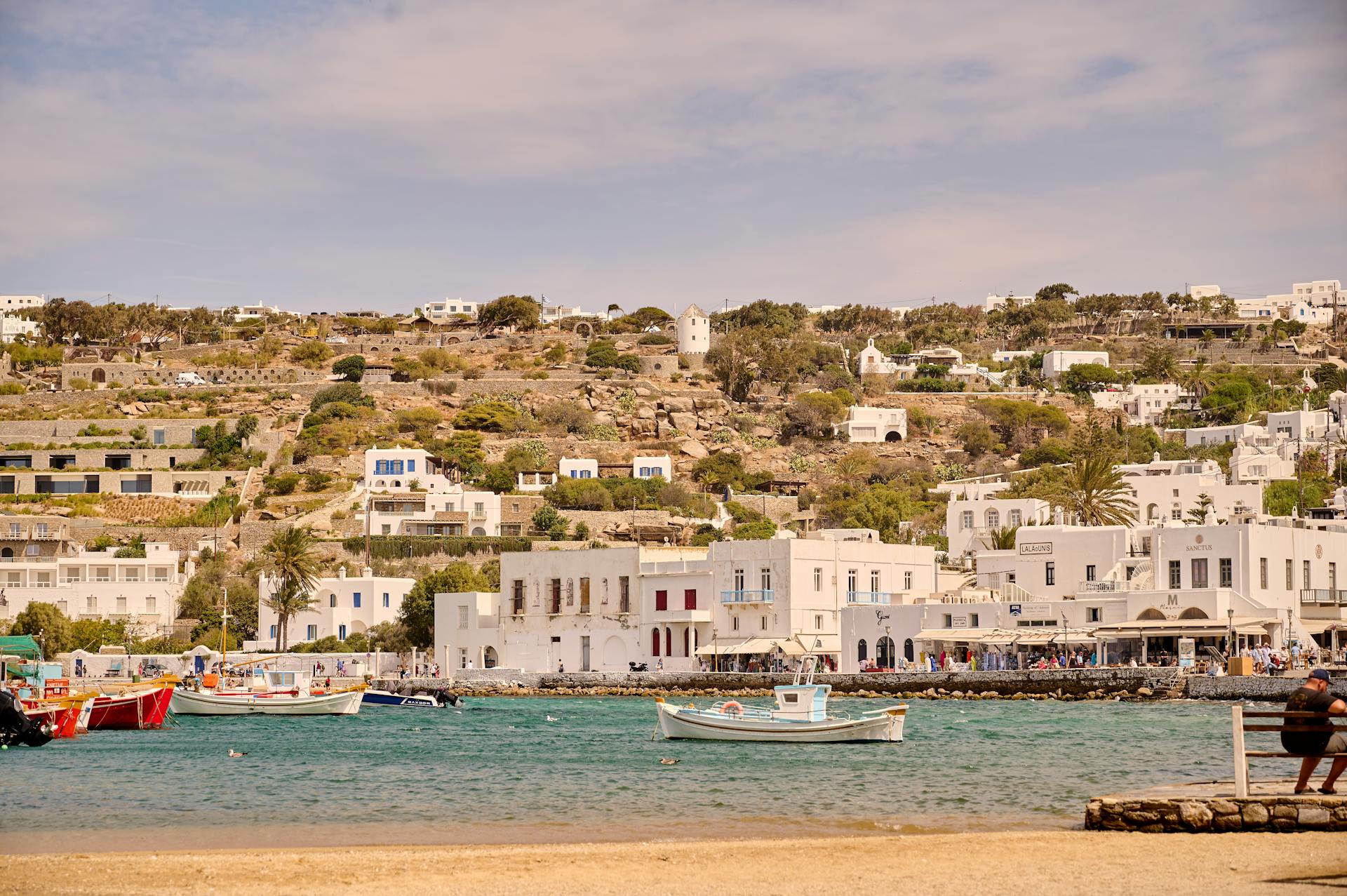 Picturesque view of Mykonos town with white buildings and boats by the sea.