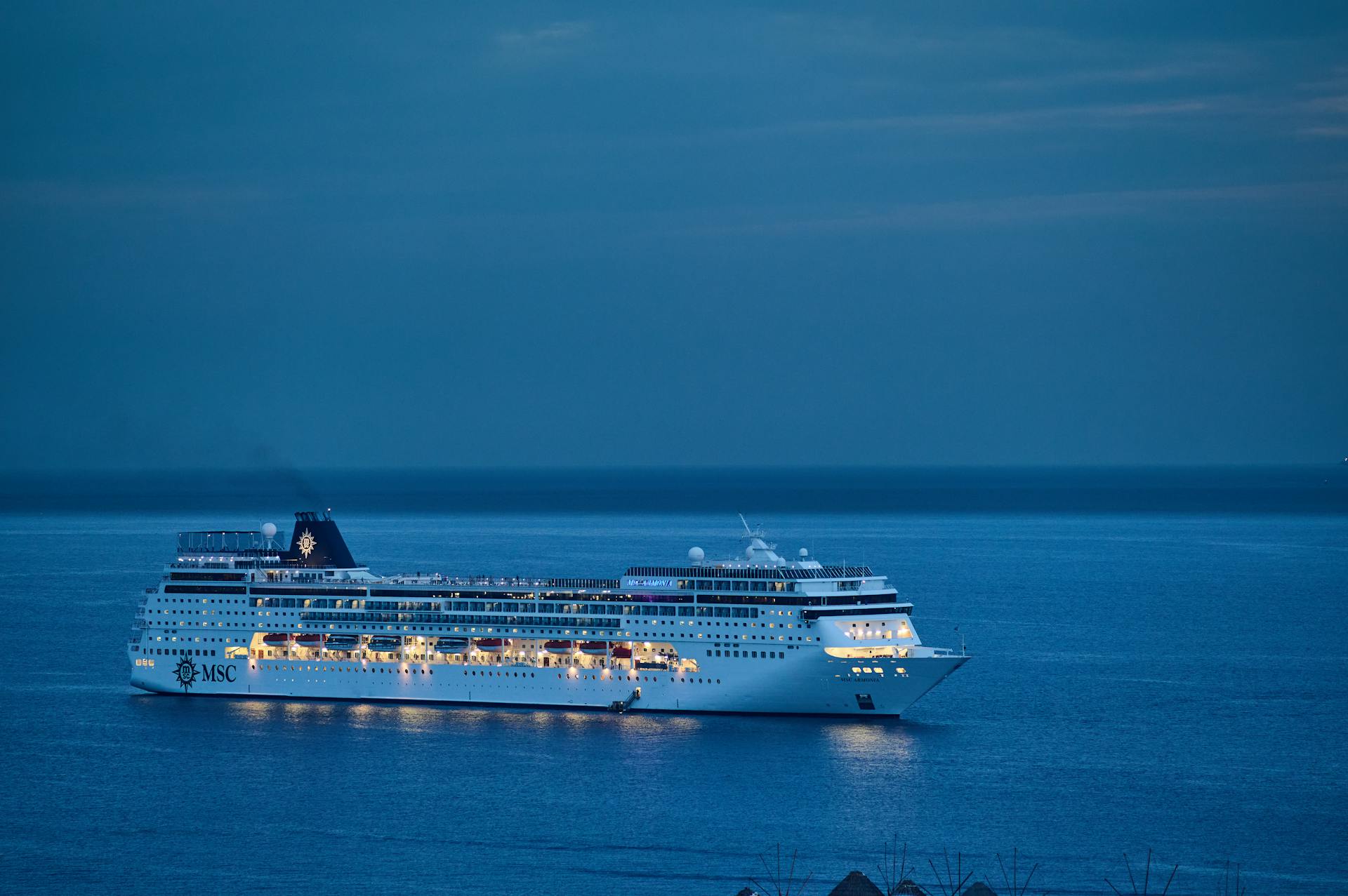 A cruise ship glides through calm waters at dusk, illuminated against the serene evening sky.