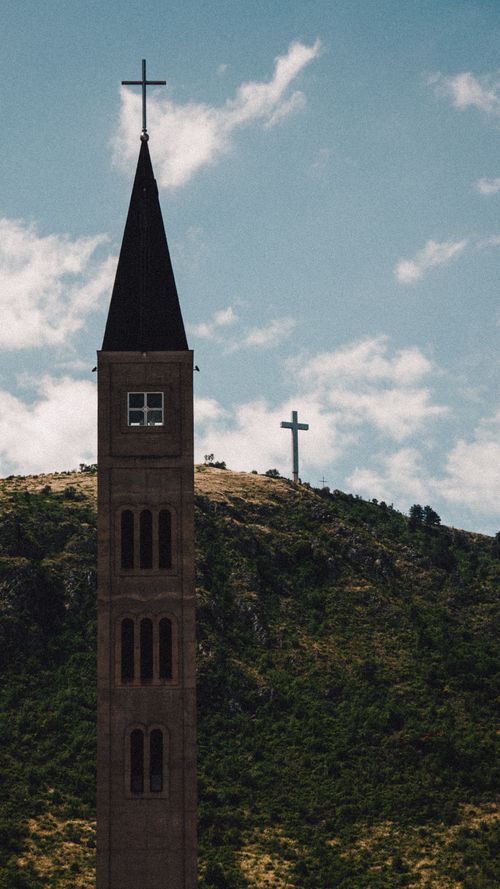 Free Vertical shot showcasing the Franciscan Church tower against a mountain backdrop in Mostar, Bosnia and Herzegovina. Stock Photo