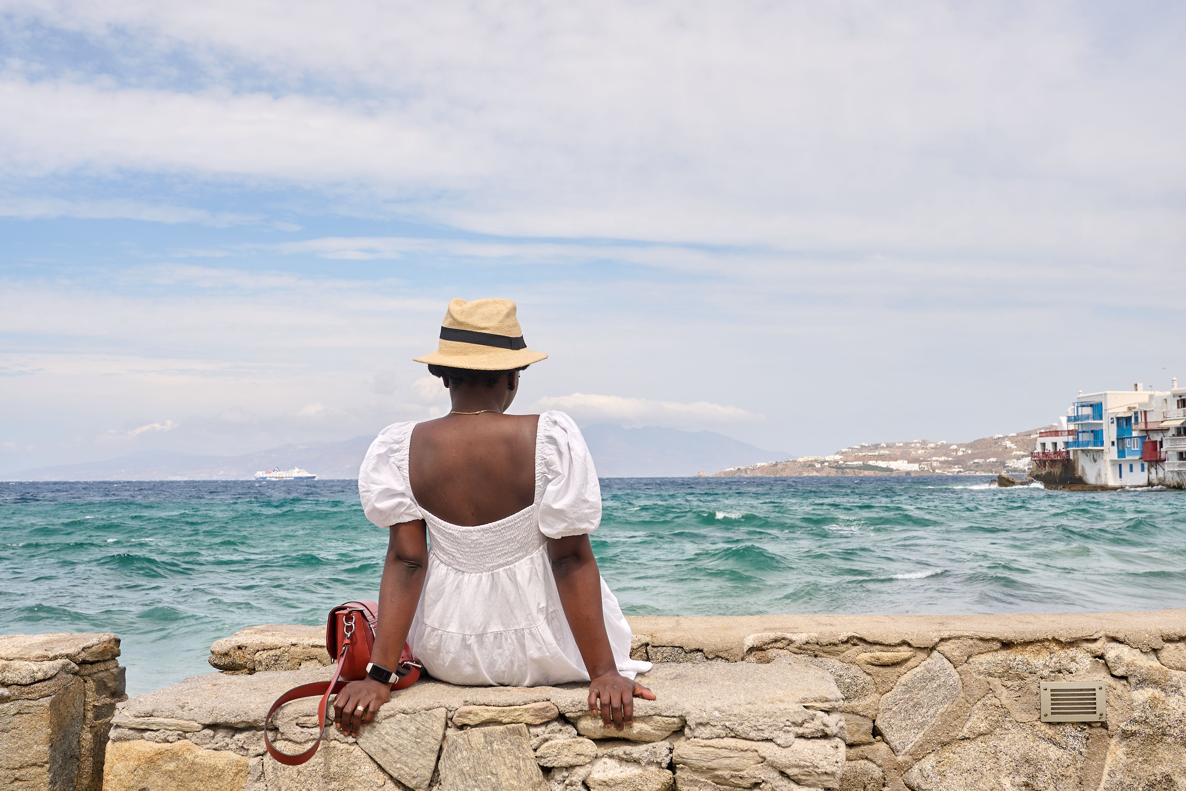 Woman in a white dress and hat enjoying the seaside view, capturing summer vibes.