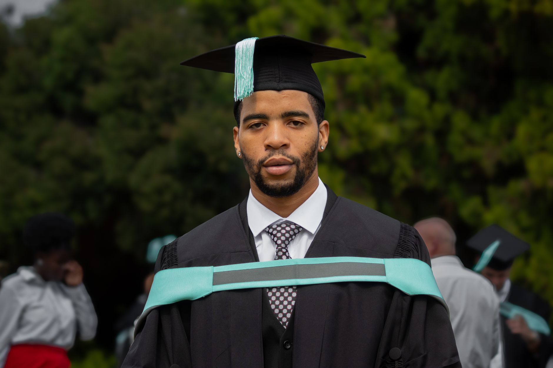 A young man in a graduation gown and cap poses outdoors in Pretoria.