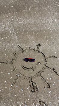 Artistic sun drawing in sand with sunglasses on a sunny beach day.