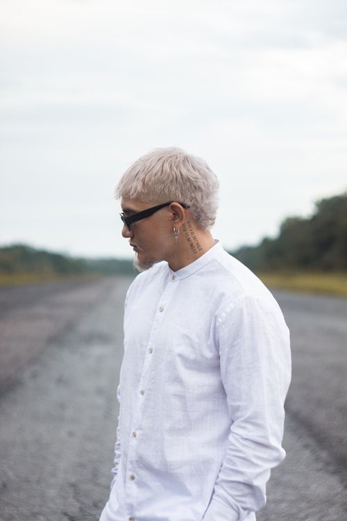 Free Fashionable young man with blonde hair on a rural road in Breves, Brazil, wearing sunglasses and a white shirt. Stock Photo