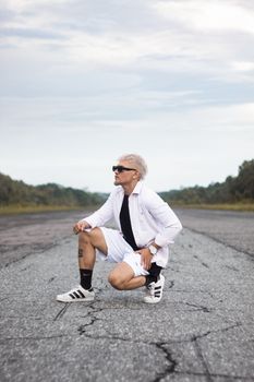 Stylish man with sunglasses poses on a rural road, showcasing a casual fashion look.