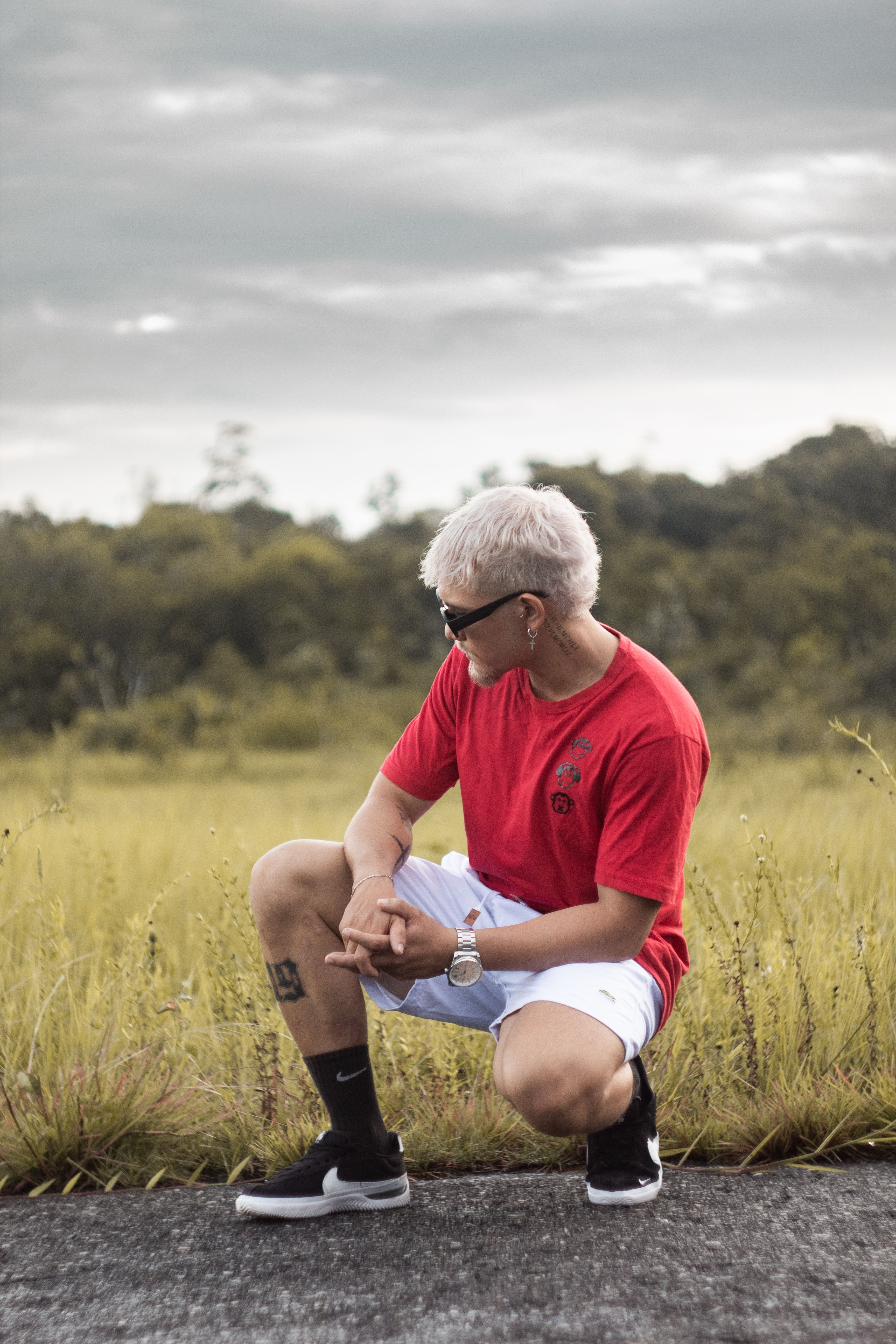Fashionable man with blonde hair crouching on a rural road, conveying a modern vibe.