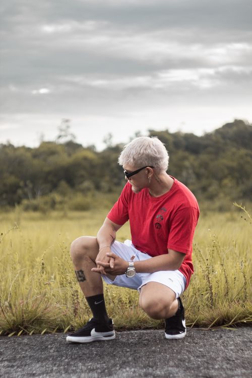 Free Fashionable man with blonde hair crouching on a rural road, conveying a modern vibe. Stock Photo